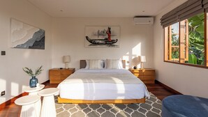 Une chambre avec un grand lit, deux tables de chevet, une fenêtre donnant sur un paysage verdoyant et des œuvres d’art accrochées aux murs.