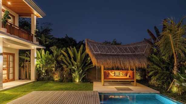 Une maison moderne dotée d’une piscine, d’un espace détente agrémenté d’un toit de chaume et d’une végétation tropicale luxuriante.