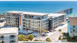 Un hôtel à plusieurs étages, doté d’une architecture moderne, situé près d’une plage et d’une jetée.