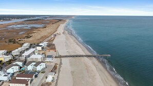 Vue aérienne d’une zone côtière avec une plage, une jetée et des immeubles résidentiels.
