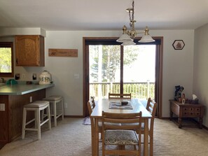 A dining area with a wooden table, chairs, and a kitchen counter with a sink and a kettle.