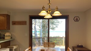 Un coin repas avec une table en bois, des chaises et une vue sur l’océan, accessible par une porte coulissante.
