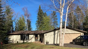 Une maison de plain-pied avec un garage, entourée d’arbres et avec un VUS garé devant.