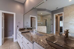 A modern bathroom with a large mirror, double sinks, and a walk-in shower.