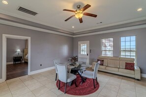 A spacious living room with a dining area, a ceiling fan, and large windows.