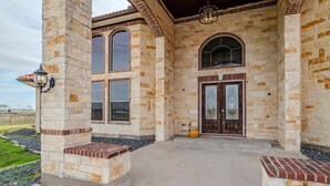 A stone building with a covered entrance, large windows, and a concrete patio. - 8BR Ranch house perfect for large families/groups (Rosharon)