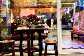 Een restaurantinterieur met een glazen scheiding, houten tafels en een bloemstuk.