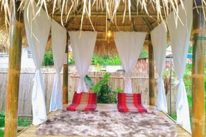 Un espace extérieur abrité, doté d’un toit de chaume, de rideaux blancs et d’un tapis en fourrure.