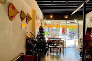 A restaurant interior with a Christmas tree, tables, chairs, and a view of the street outside. - Hug Pai Garden City Retreat (Pai)