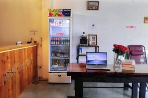 Un espace d’accueil avec un comptoir en bois, un réfrigérateur rempli de boissons, un ordinateur portable posé sur une table et un vase avec des fleurs rouges.
