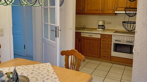A kitchen with wooden cabinets, a stove, and a dining area with a table set for two. - Vacation apartment no. 2 for 1 - 4 persons 59 sqm (Reit im Winkl)