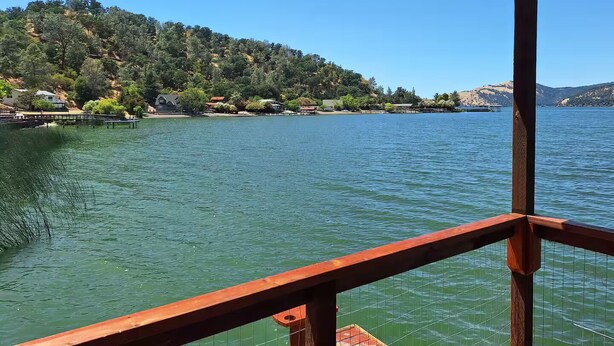 A lakeside view from a wooden deck with a clear view of the water, surrounding hills, and distant mountains. - Waterfront 3-bedroom house in Clearlake Park with private dock (Clearlake Park)