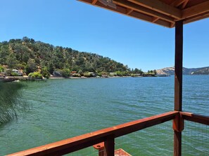 Vista panorámica sobre un lago desde una terraza de madera, con agua cristalina, colinas circundantes y montañas distantes.