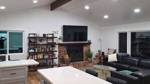 A spacious living area with a stone fireplace, a flat-screen TV, a black leather sofa, and a kitchen area with a white countertop and grey cabinets. - Waterfront 3-bedroom house in Clearlake Park with private dock (Clearlake Park)