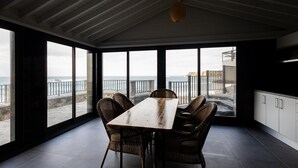 A dining area with a large table and wicker chairs, overlooking a coastal view through large windows. - GuestReady - beachfront retreat in Porto Formoso (Porto Formoso)