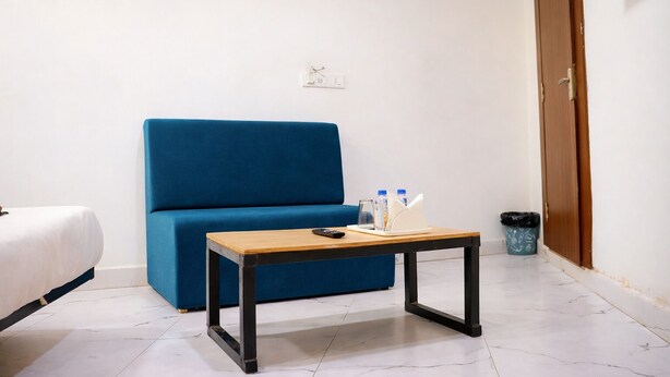 A room with a blue sofa, a small wooden table with a remote control, and a trash bin. - Kanha Inn (Bhopal)