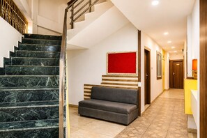 Un hall d’hôtel avec un escalier en marbre, un canapé, un mur d’accent rouge et une porte en bois.