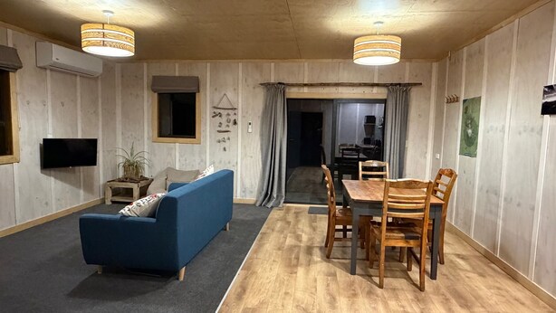 Ein Zimmer mit einem blauen Sofa, einem Holzespeisetisch und Stühlen, sowie einem Fernseher und einer Klimaanlage an der Wand.