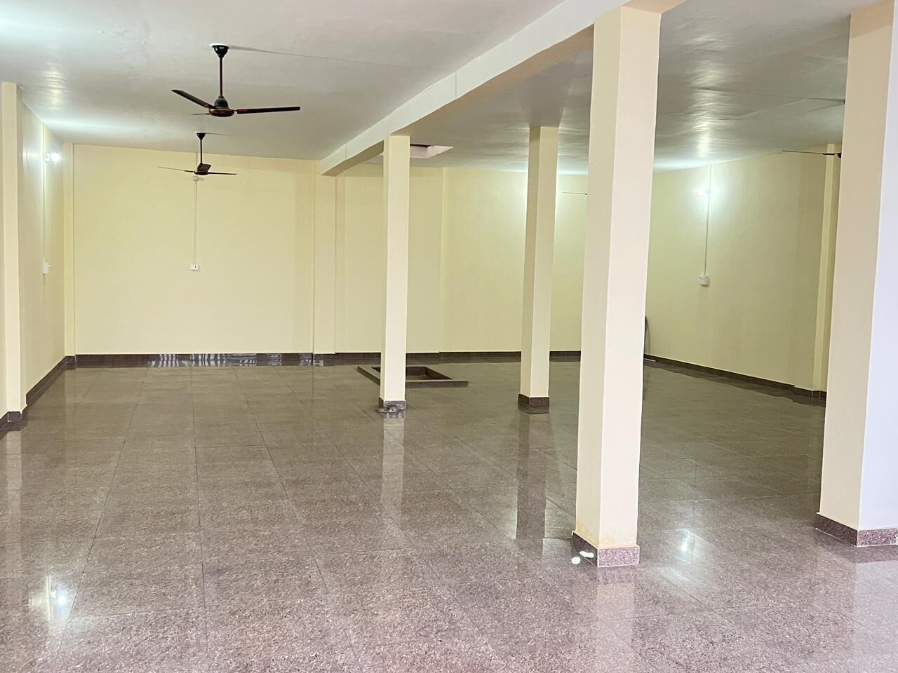 A spacious room with a polished floor, ceiling fans, and columns.