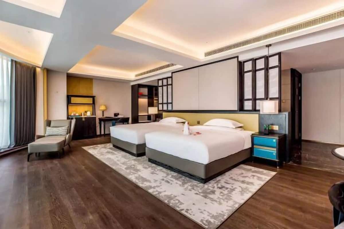 A modern hotel room with two beds, a desk, and a seating area.