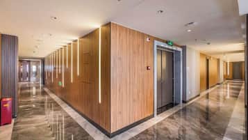 A hotel corridor with wooden paneling, a marble floor, and an elevator.