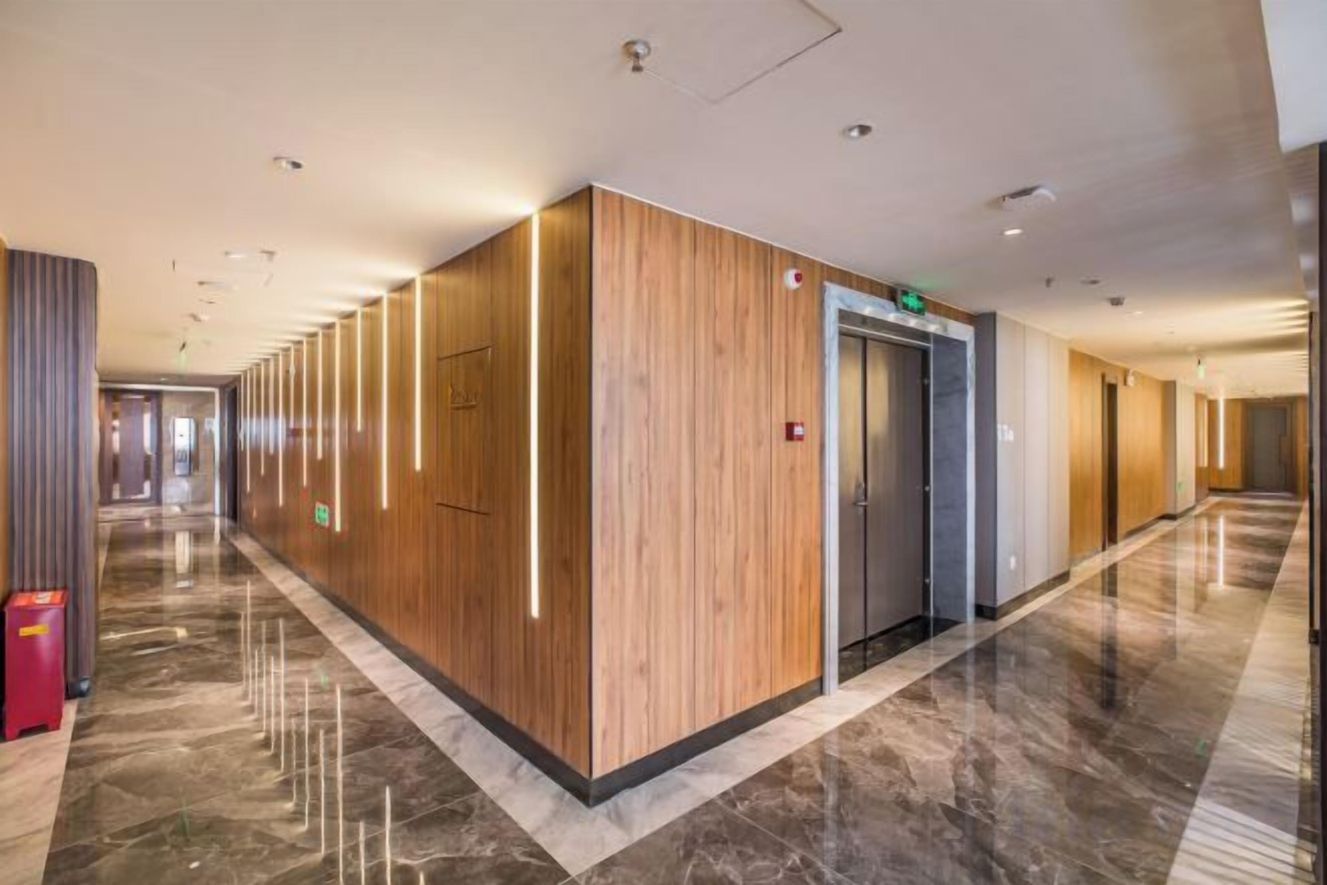 A hotel corridor with wooden paneling, a marble floor, and an elevator.
