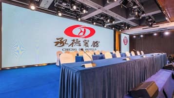 A conference room with a long table, chairs, and a presentation screen with hotel branding.
