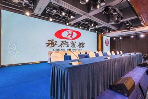 Une salle de conférence équipée d’une longue table, de chaises et d’un écran de présentation arborant le logo de l’hôtel.