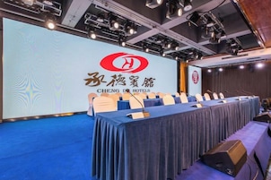 Una sala de conferencias con una larga mesa, sillas y una pantalla de presentación con la marca del hotel.