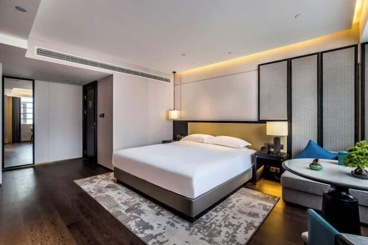A modern hotel room with a large bed, bedside tables, a round table, and a small plant.