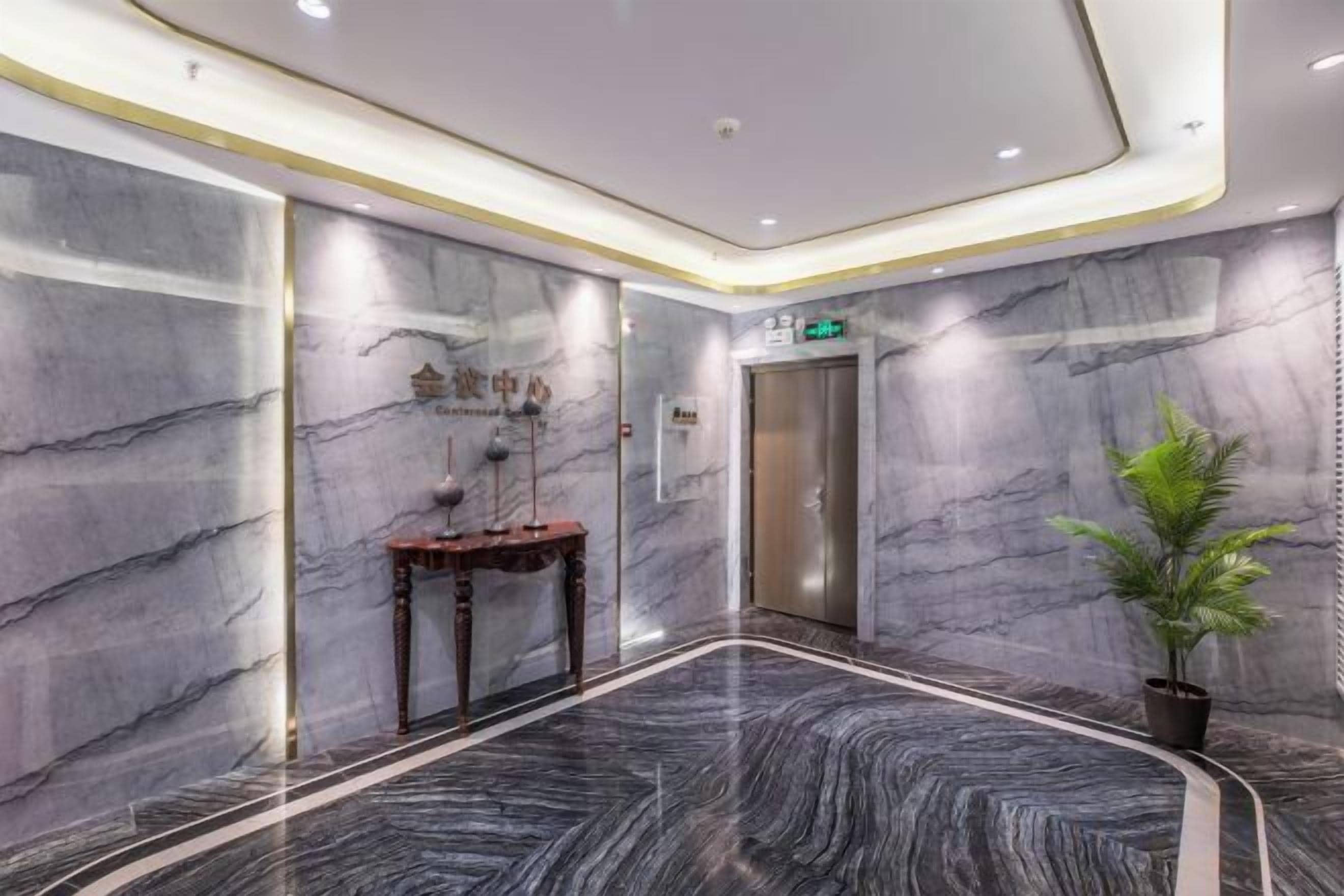 A modern elevator area with marble walls, a potted plant, and a small table with a vase.