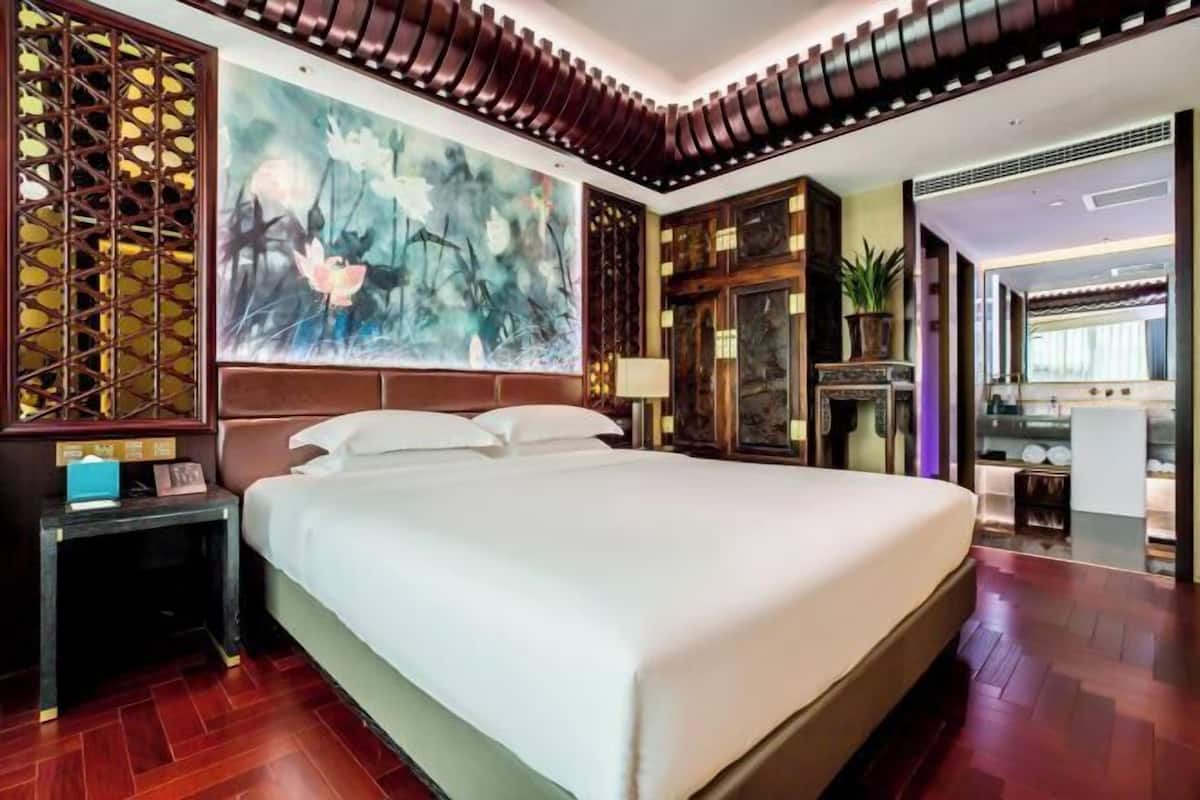 A large bed with a headboard, a nightstand, a wall-mounted lamp, and a large abstract painting.