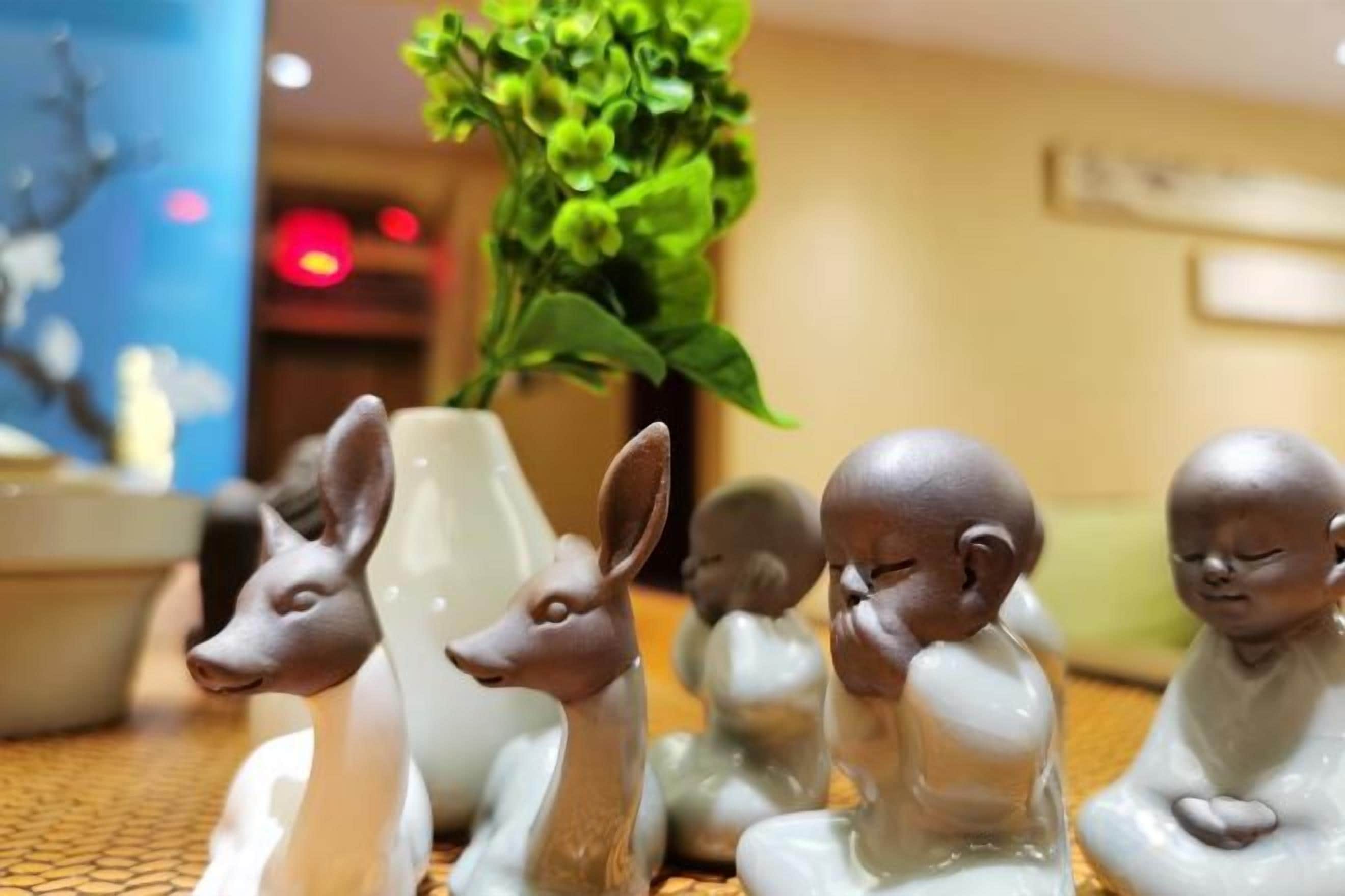 Una mesa con figuritas de cerámica, un florero con plantas verdes y un fondo desenfocado con un letrero.