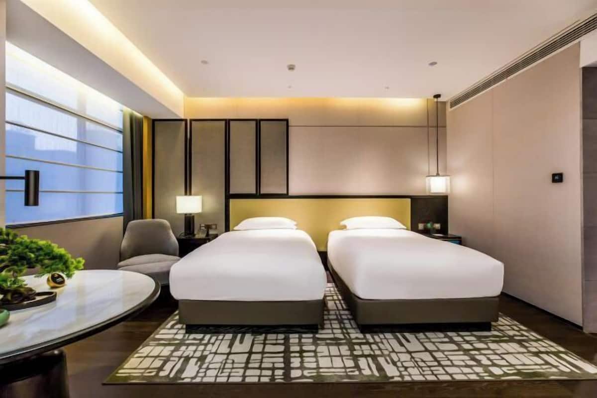 A hotel room with two beds, a desk, a chair, and a large window.