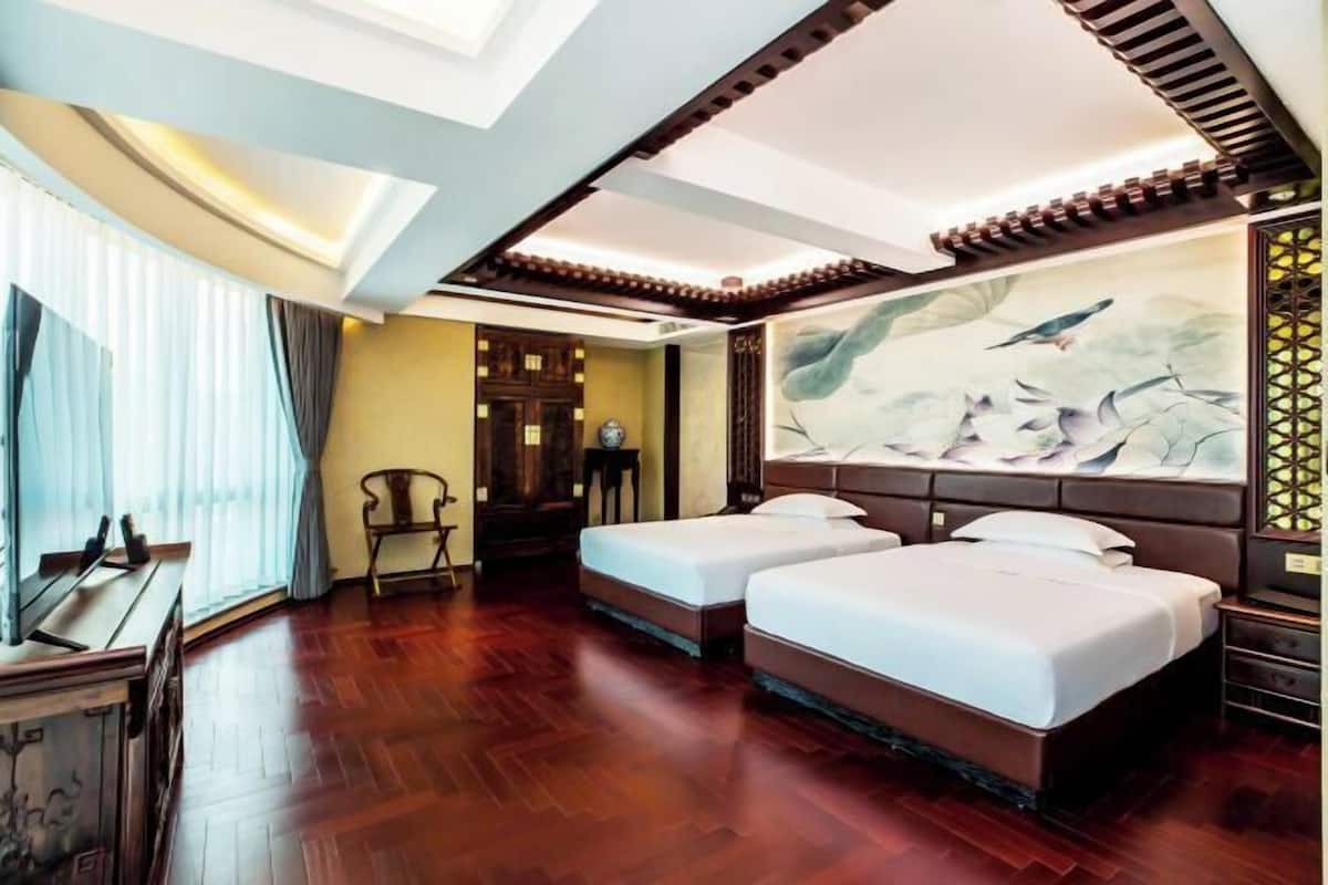 A hotel room with two beds, wooden flooring, a large painting, and a traditional-style ceiling.