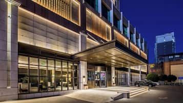 Une entrée d’hôtel moderne avec un passage couvert, de grandes fenêtres et un espace de stationnement.