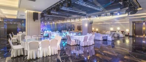 Un amplio salón de banquetes con mesas y sillas redondas, un piso de mármol pulido y un techo alto con iluminación escénica.