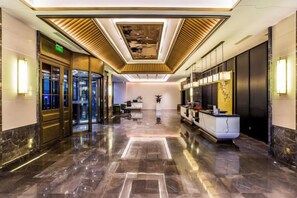 Un vestíbulo de hotel con una recepción, una zona de estar y un diseño moderno de techo.