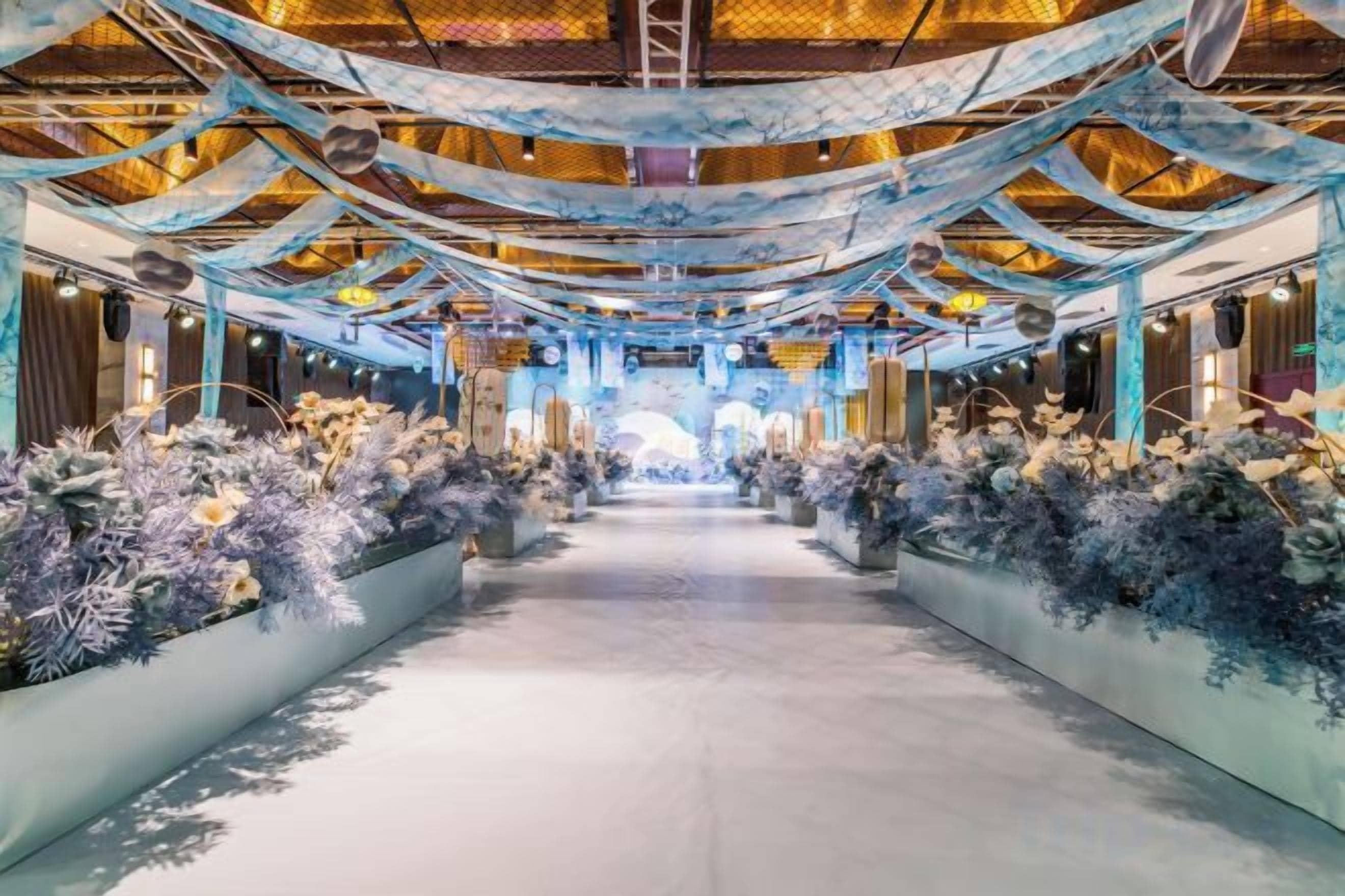 A corridor with floral arrangements on either side, leading to a bright area at the end.