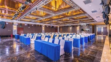 A conference room with rows of tables and chairs, a polished floor, and a high ceiling with lighting fixtures.