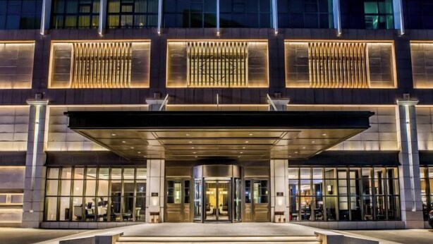 Una entrada de hotel moderna con puerta giratoria, ventanas amplias y un área de acceso cubierta.