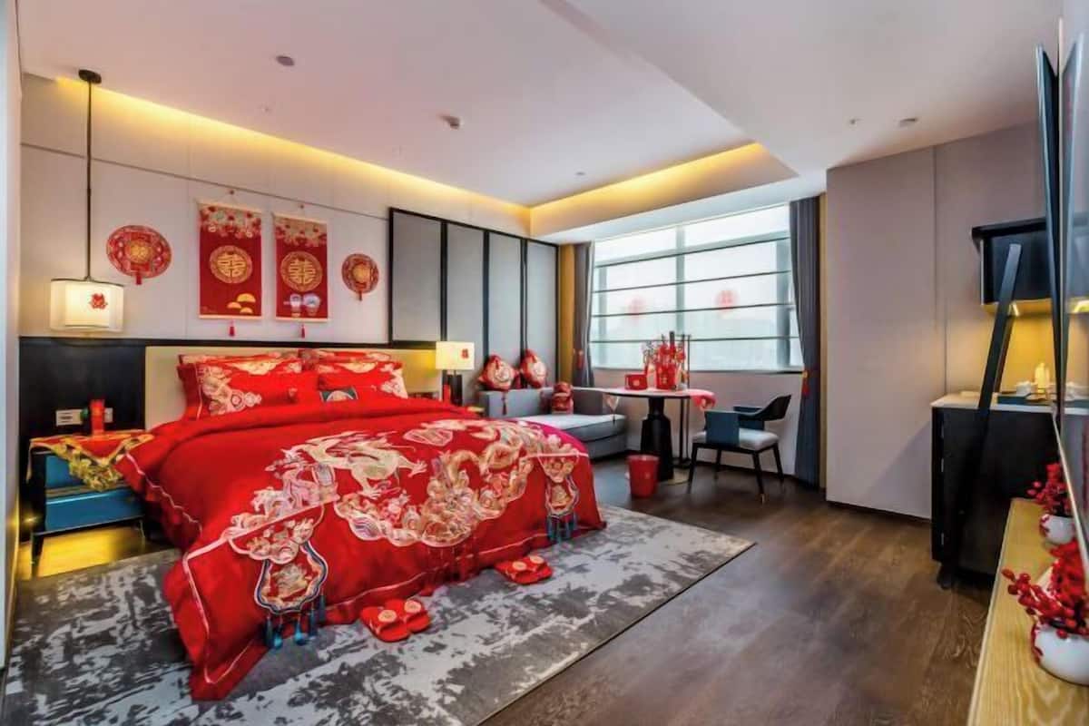 A modern bedroom with a large bed, a desk, and a window.
