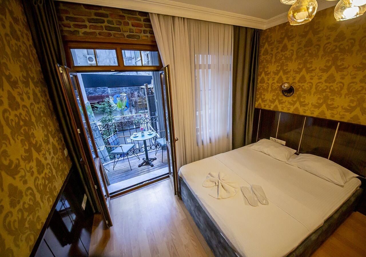 Quarto de hotel com cama, vista para um pátio com mesas e cadeiras, e uma varanda.