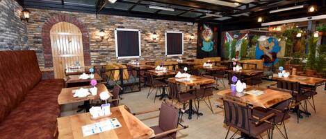 A restaurant with wooden tables and chairs, stone walls, and a mural.