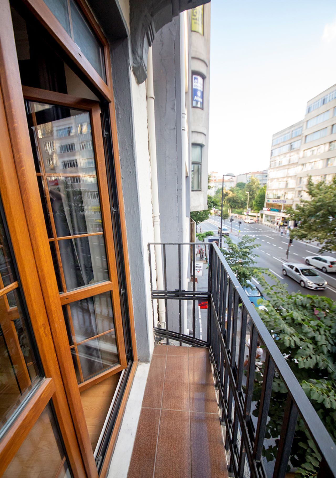 A balcony with a view of a street, a building with a sign, and a window with a view of another building.