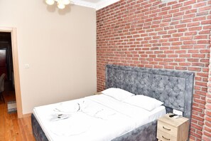 A bedroom with a brick wall, a tufted headboard, a wooden nightstand, and a bed with white linens. - Royal Garden Suite Hotel (Istanbul)