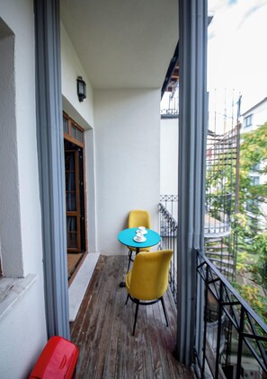 A balcony with a table and chairs, a red suitcase, and a view of a building and greenery. - Royal Garden Suite Hotel (Istanbul)