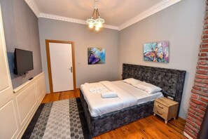 A bedroom with a bed, a TV, a door, and two paintings. - Royal Garden Suite Hotel (Istanbul)