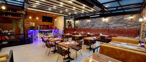A restaurant with a glass ceiling, wooden tables and benches, and a stone wall.