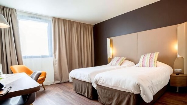 A hotel room with a double bed, a desk with a chair, a window with curtains, and a bedside table with a lamp. - Campanile Aubagne - Alta Rocca (Aubagne)